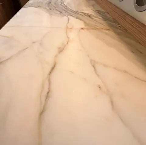 Plan de travail en pierre blanche veinée sur des meubles de cuisine en bois.