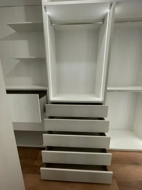 Dressing blanc avec colonne de tiroirs ouverts, penderie éclairée par LED et étagères.