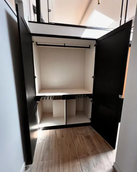 Dressing aux portes noires ouvertes sur une penderie éclairée.
