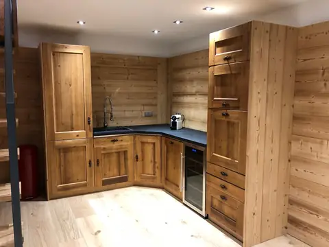 Cuisine d'angle aux façades en bois vieilli, plan de travail noir, cave à vin et colonnes de rangement.