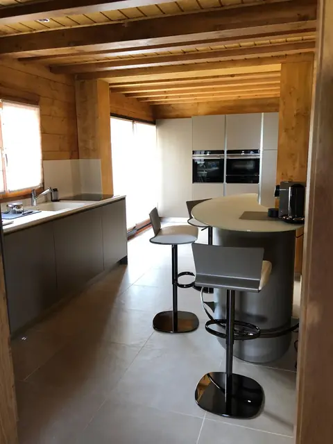Cuisine moderne sous plafond en bois, avec colonnes grises, plan de travail et îlot rond entouré de tabourets.